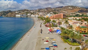 A coastal town with a beach, buildings, and mountains in the background. - Arrayanes Playa Hotel (Almunecar)