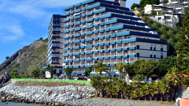 A multi-story hotel with balconies, located near a rocky shoreline with palm trees. - Arrayanes Playa Hotel (Almunecar)