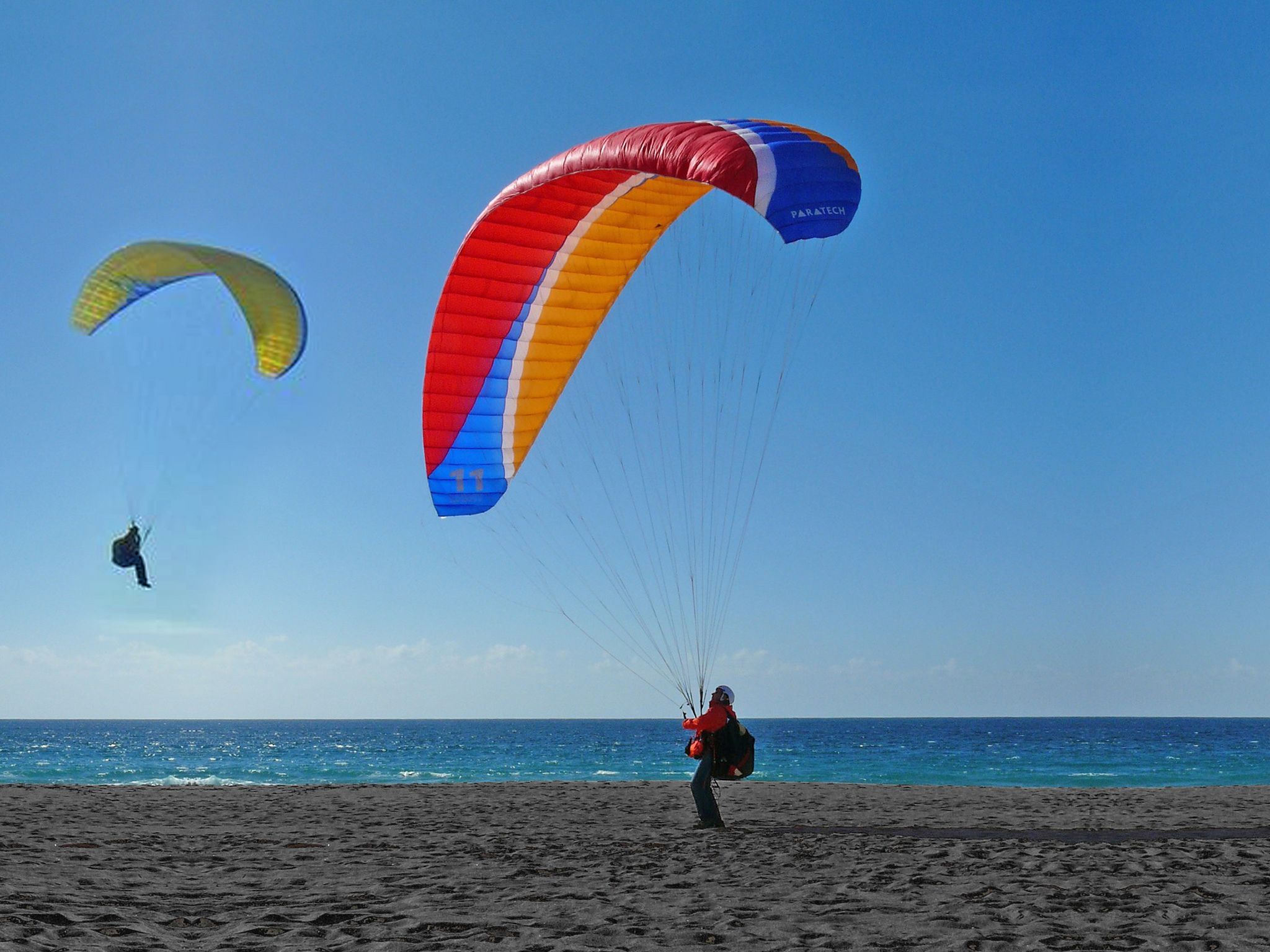 A beach with two parachutes and a person standing on the sand.