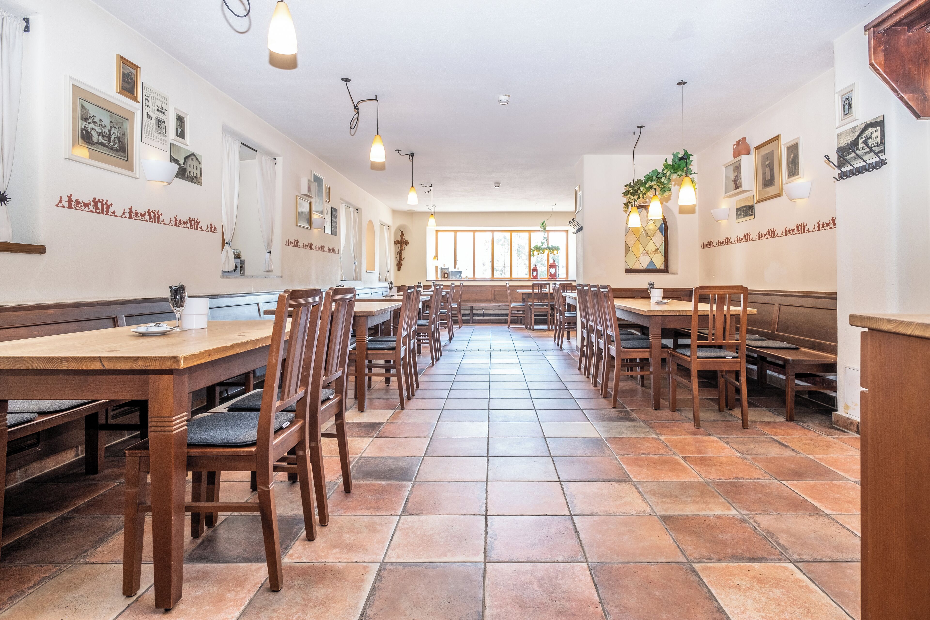Une grande salle à manger avec des tables et des chaises en bois, de grandes fenêtres et des luminaires fixés au mur.