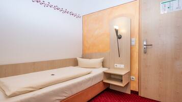 Una cama individual con cabecera de madera, una mesita de noche y un aplique de pared.