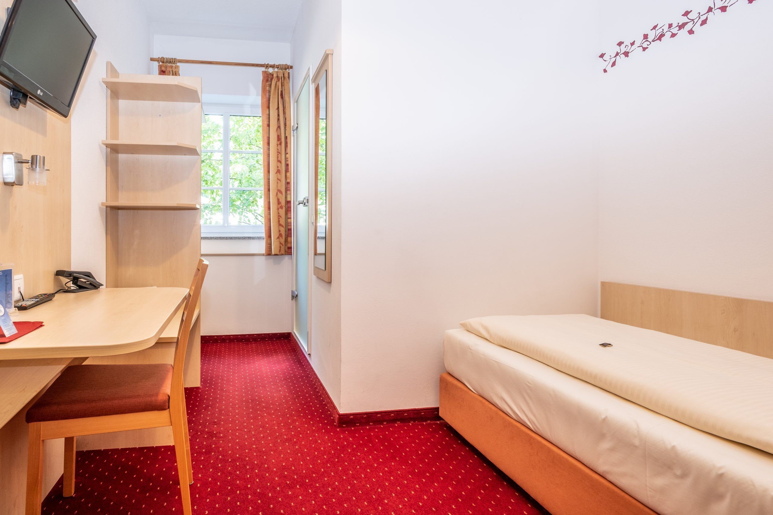 A small, neatly arranged room with a bed, a desk, and a chair.