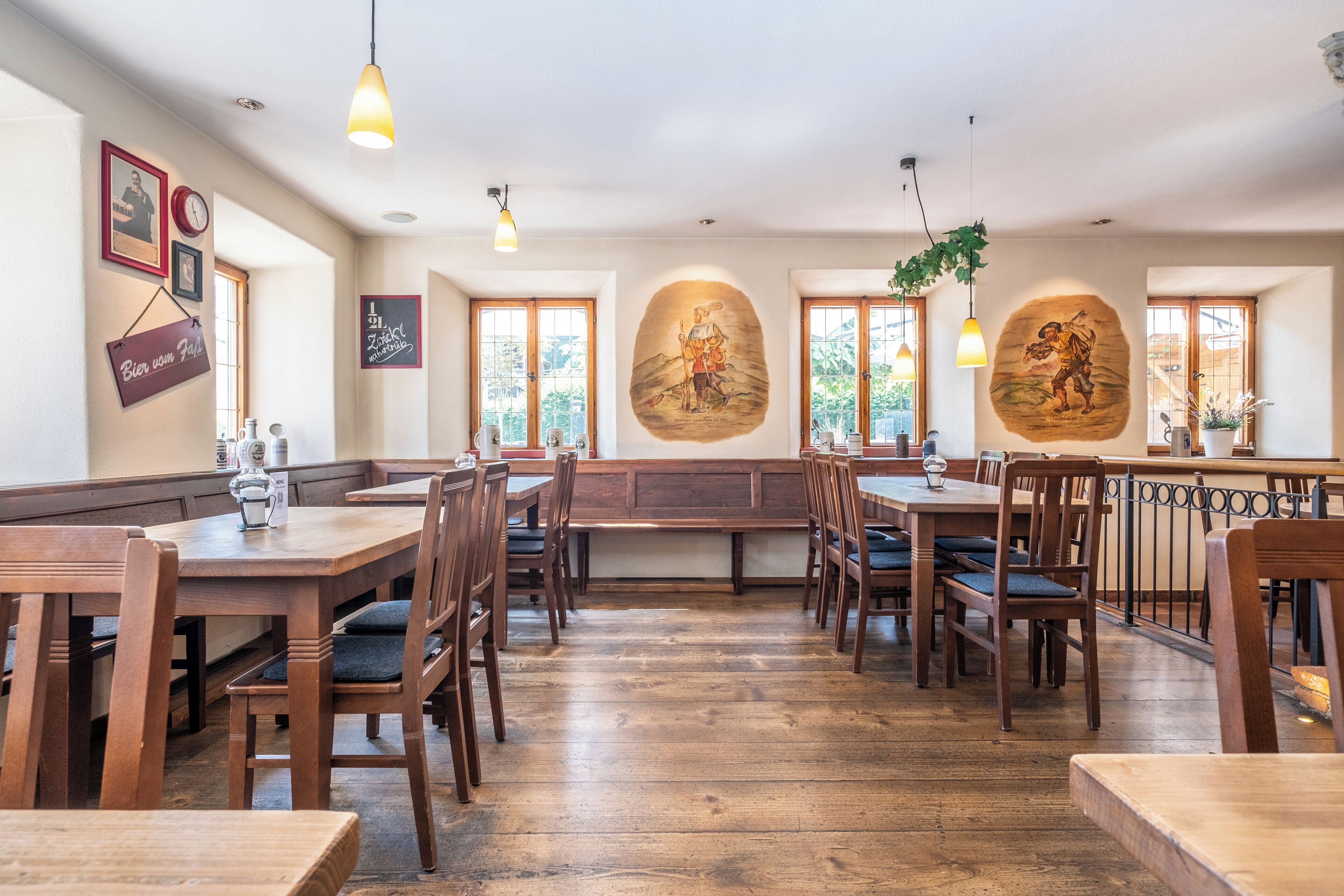 Un ristorante con tavoli e sedie in legno, ampie finestre e decorazioni alle pareti.