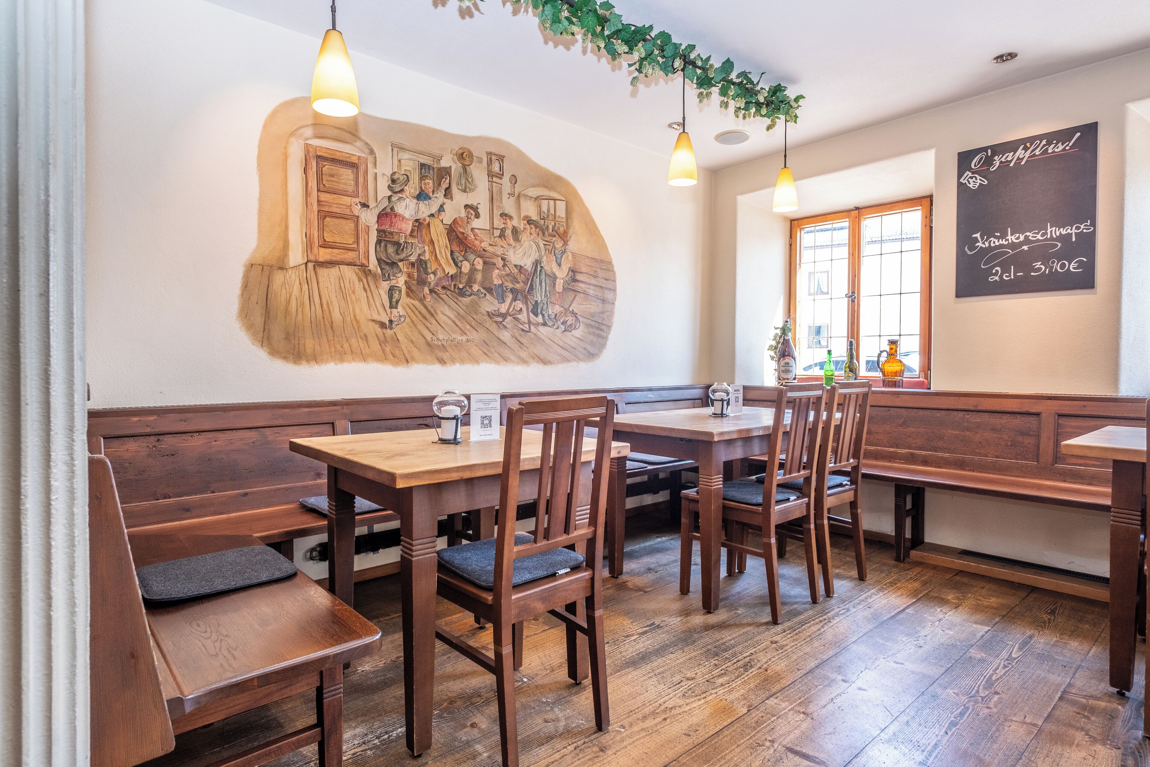 L’intérieur d’un restaurant est aménagé avec des meubles en bois, une fresque murale et un menu écrit à la craie sur un tableau noir.