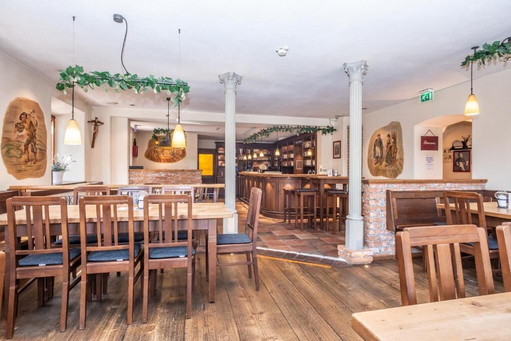 A restaurant interior with wooden tables and chairs, hanging lights, and decorative wall art.