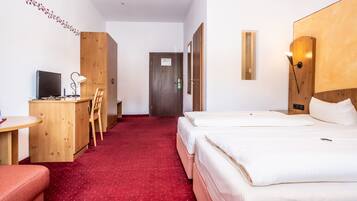 A hotel room with a desk, chair, two beds, a red carpet, and a wooden wardrobe.