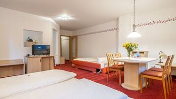 Una habitación de hotel con cama, escritorio, silla, televisor y una mesita con un florero.