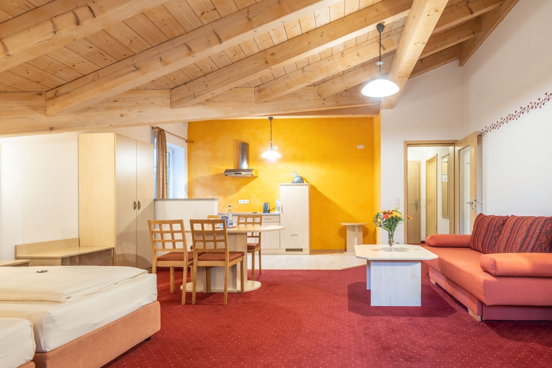 Una habitación acogedora con techo de madera, un comedor con sillas y una mesa, un sofá y una pequeña cocina con estufa y armarios.