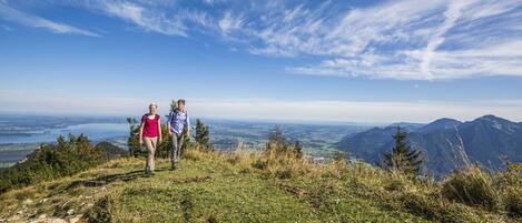 Zwei Personen stehen auf einer grasbewachsenen Anhöhe mit Blick auf ferne Berge und ein Tal.