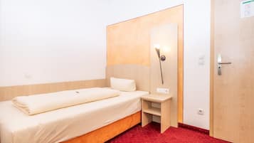 Una habitación pequeña y ordenada con una cama individual, una mesita de noche, una lámpara de pared y una puerta.