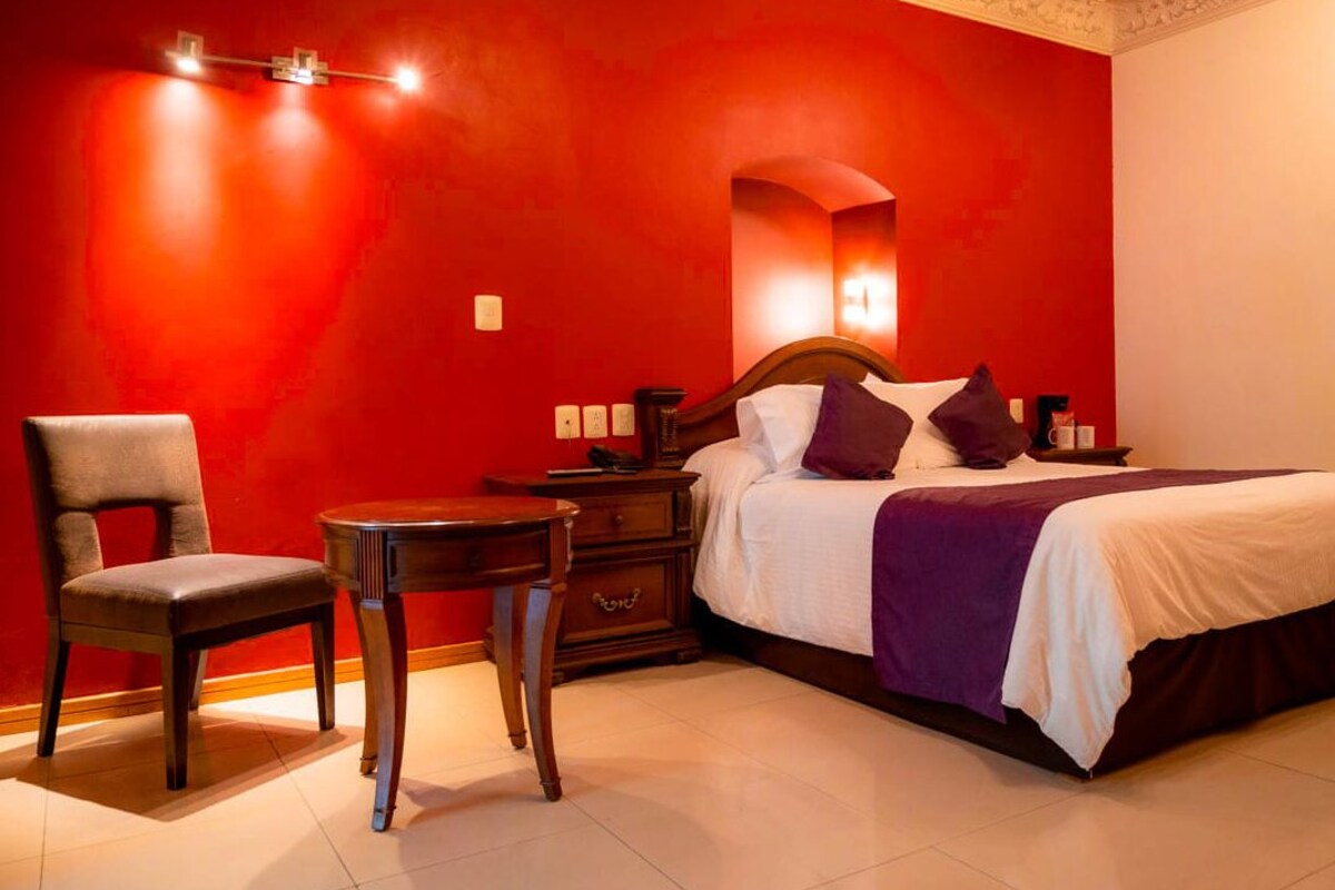 Une chambre à coucher comprenant un lit, une chaise, une table de chevet et un luminaire fixé au mur.
