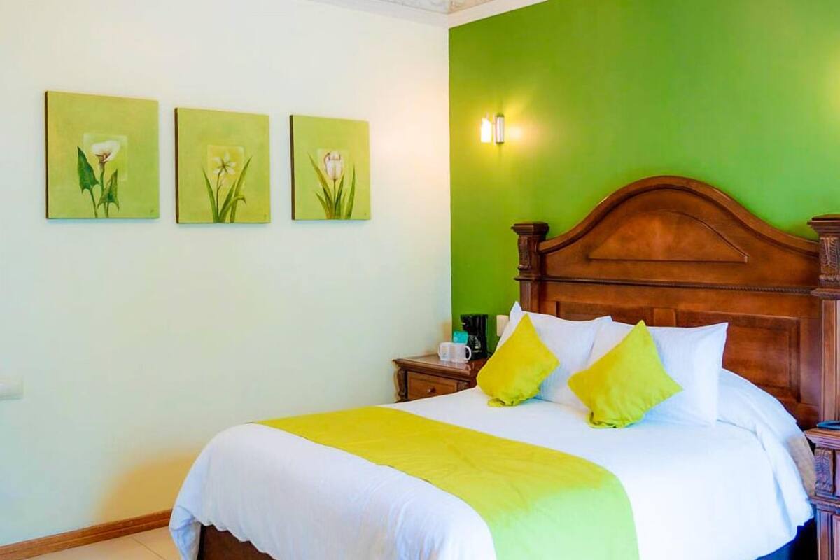 Une chambre d’hôtel avec un grand lit, des murs verts et trois appliques murales.
