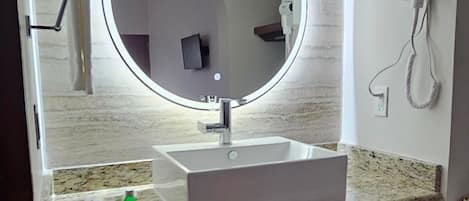 A modern bathroom with a round mirror, white sink, granite countertop, and a towel rack.