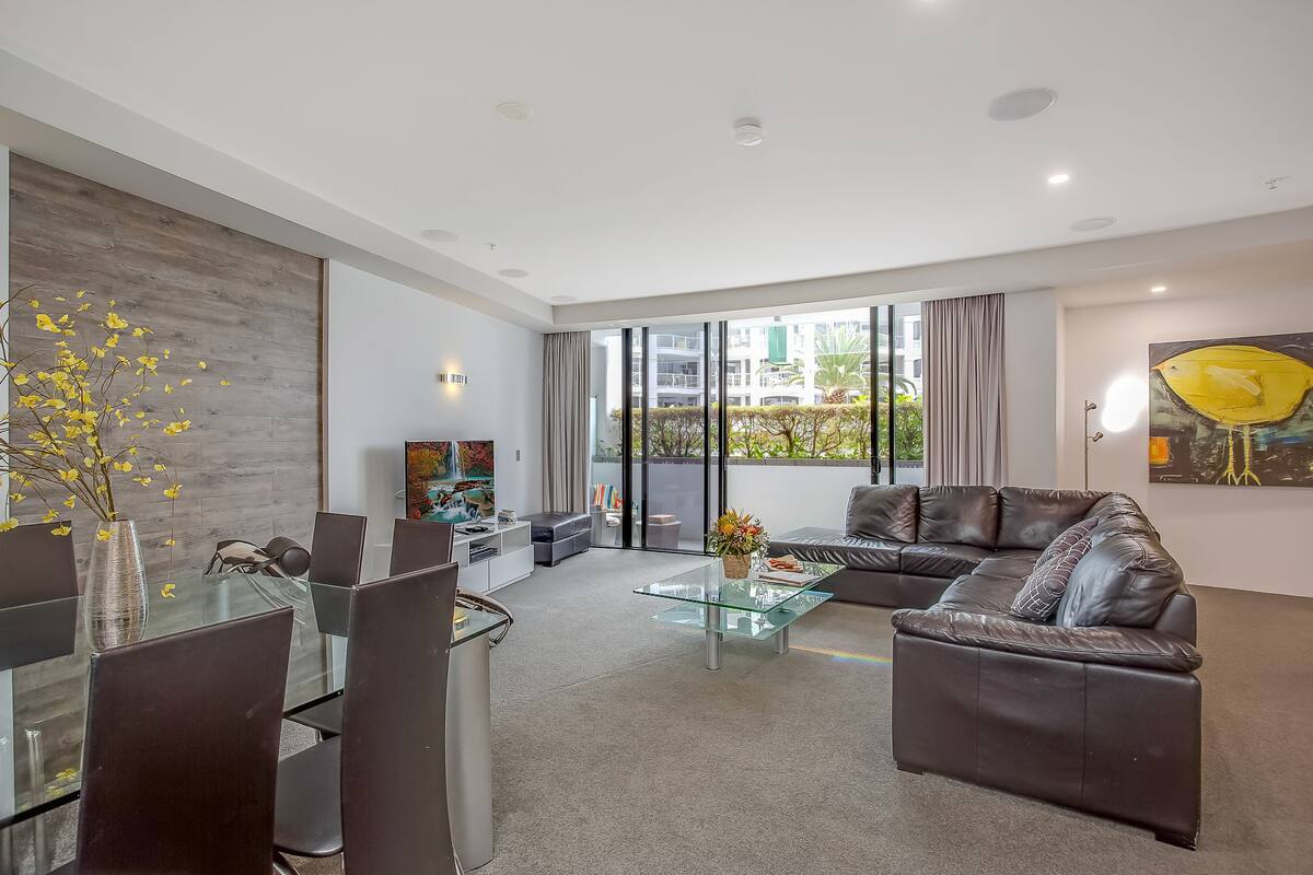 A modern living room with a glass coffee table, leather sofa, and dining area with chairs.