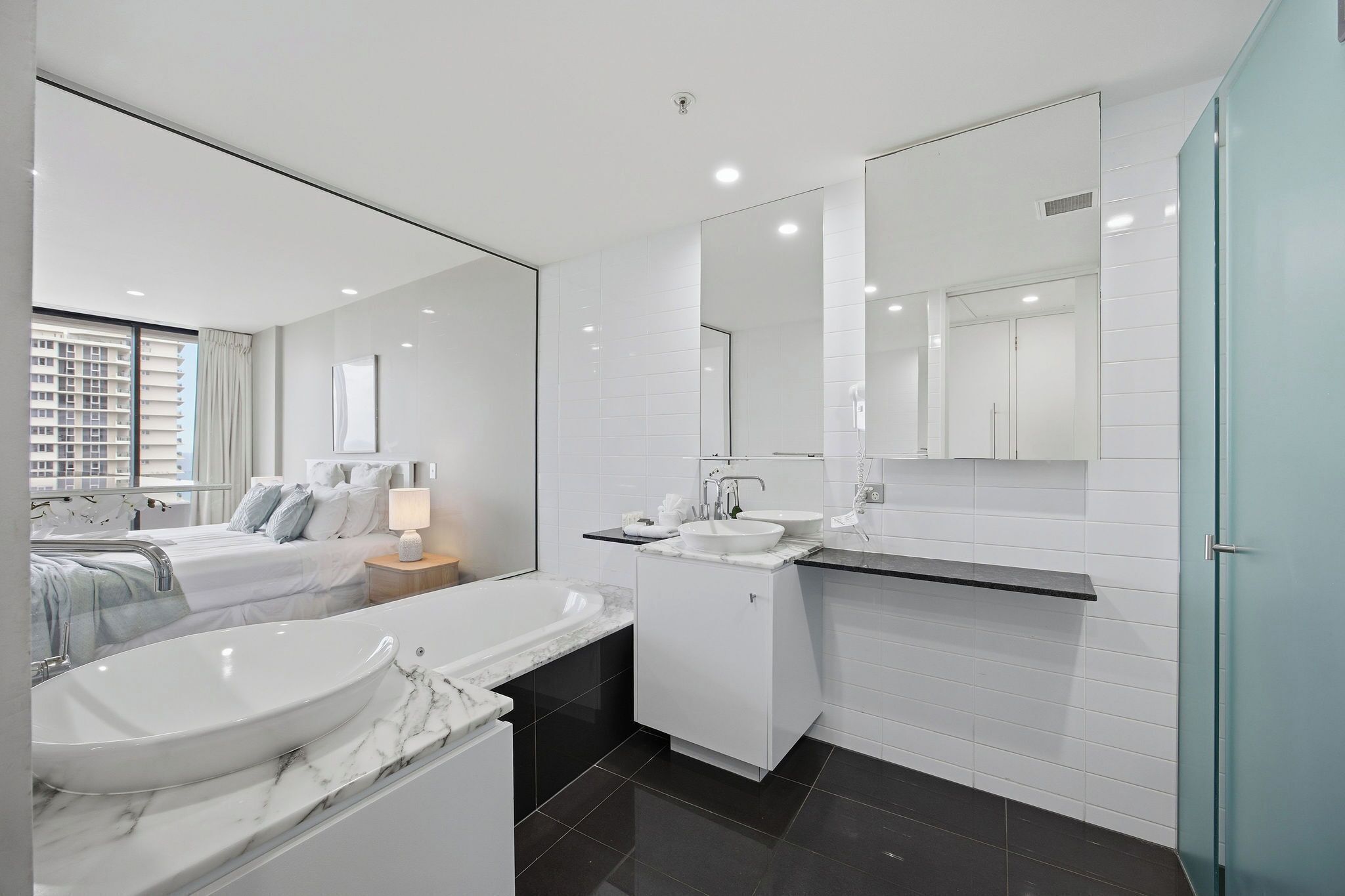 Ein modernes Badezimmer mit großem Spiegel, zwei Waschbecken, einer Badewanne und einem Fenster mit Blick auf die Stadt.