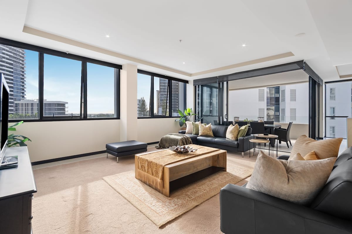 A spacious living room with a large window, a sofa, a coffee table, and a dining area.