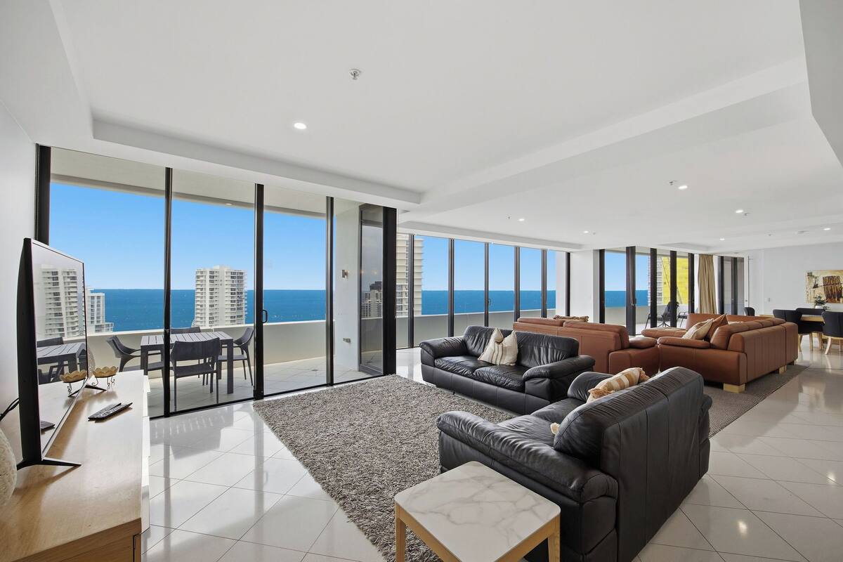 A spacious living area with a large window, a flat-screen TV, and a seating arrangement including sofas and a coffee table.