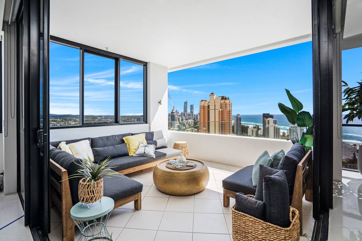 A modern living room with a city view, featuring a sofa, chairs, a coffee table, and a small side table.