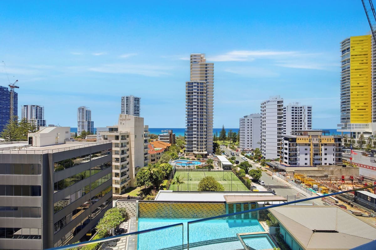 A high-rise building with a view of the ocean, a swimming pool, and a tennis court.