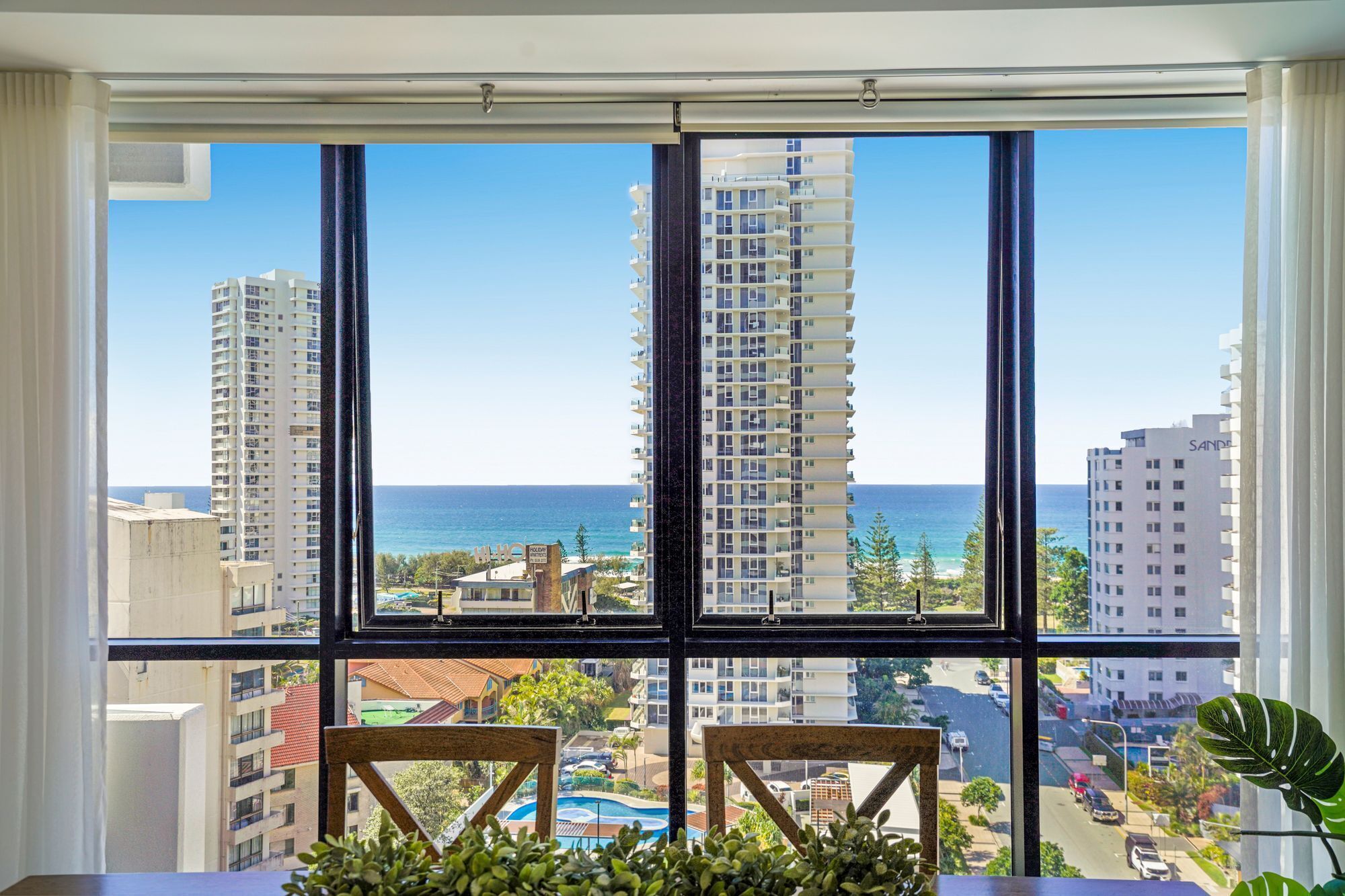 A room with a large window overlooking a cityscape, a pool, and a view of the ocean.