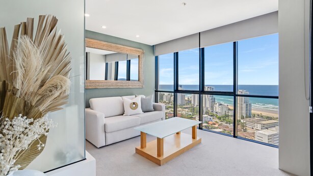 Una sala de estar moderna con un gran ventanal, un sofá blanco, una mesa de centro de vidrio y un jarrón decorativo.