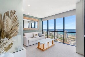 A modern living room with a large window, a white sofa, a glass coffee table, and a decorative vase. - Aria Apartments (Broadbeach)