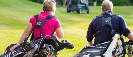 Two individuals carrying golf bags on a golf course.