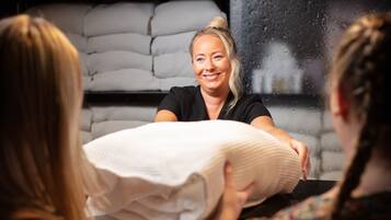 A person sitting at a table with a white pillow, in front of a window with a view of stacked mattresses.