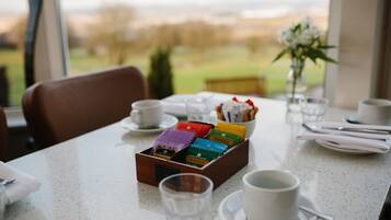 A dining table with a box of tea bags, cups, and a vase with flowers.