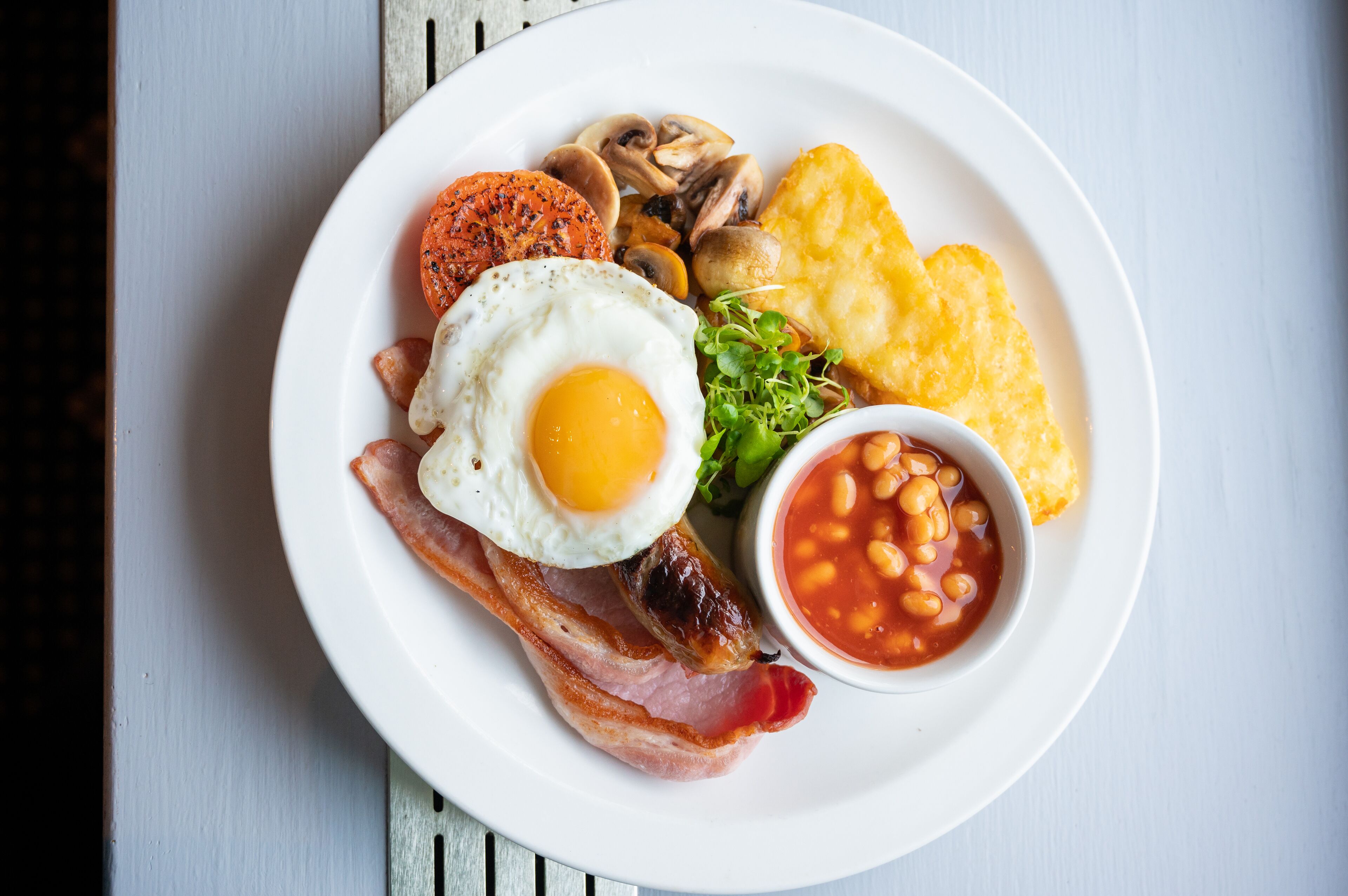 A plate of breakfast food including eggs, bacon, mushrooms, beans, and hash browns.