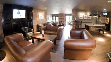A lounge area with leather sofas, a pool table, and a brick wall.