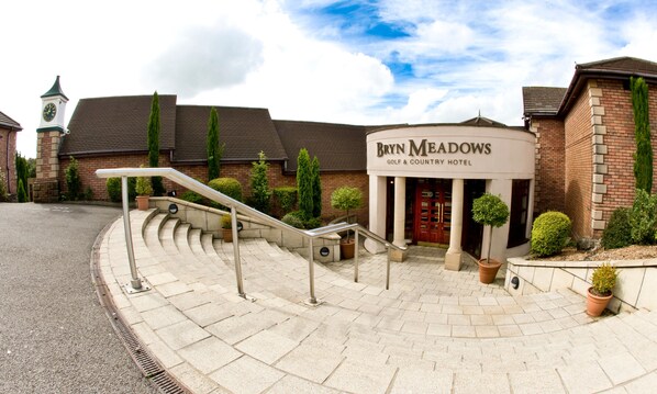 The Bryn Meadows Golf & Country Hotel with a stone staircase leading to the entrance, surrounded by potted plants and a brick building with a clock tower. - Bryn Meadows Golf, Hotel & Spa (Blackwood)