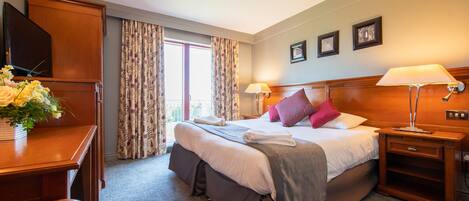 A hotel room with a large bed, bedside lamps, a desk with a TV, and a window with curtains.