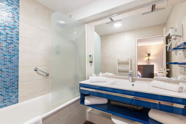 Un baño moderno con ducha envuelta en vidrio, una bañera blanca y un tocador azul con un espejo grande.