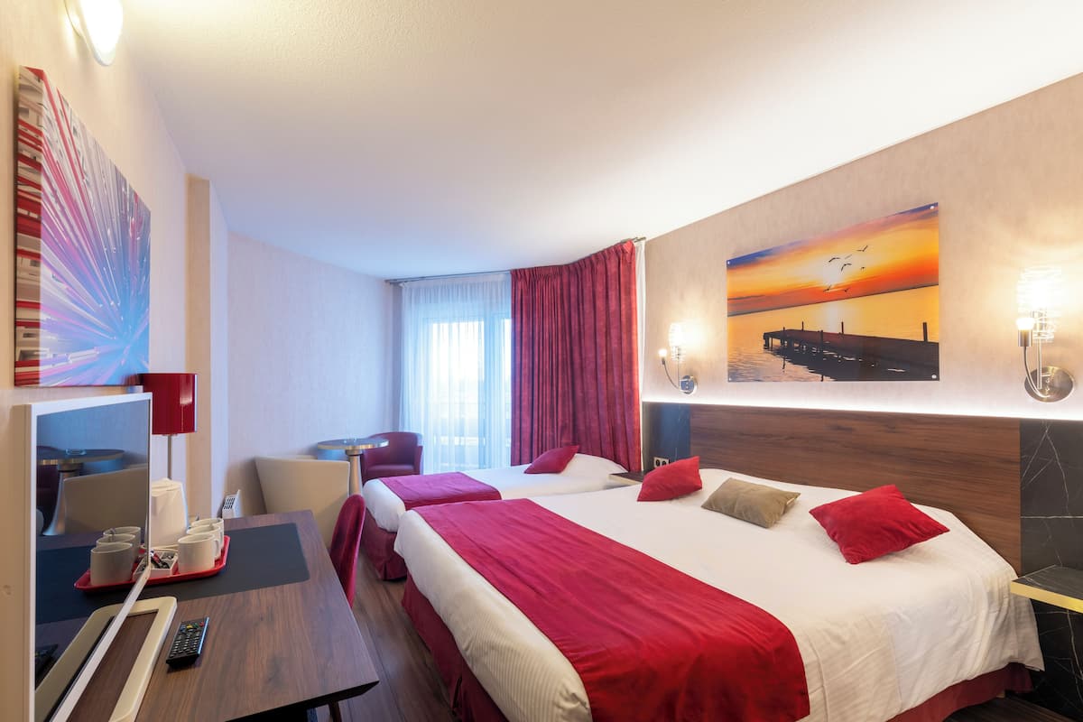 A hotel room with two beds, a desk with a chair, a TV, and a red curtain.