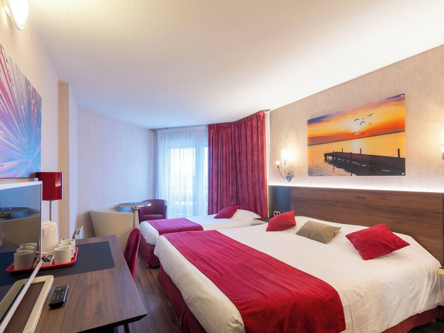A hotel room with two beds, a desk with a chair, a TV, and a red curtain.