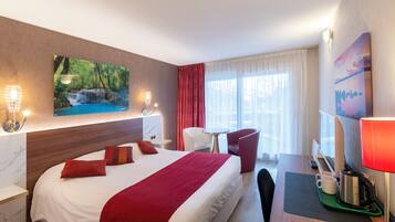 Ein Hotelzimmer mit einem großen Bett, einem Schreibtisch mit Lampe, einem Sessel, einer Kaffeemaschine und einem Gemälde einer Wasserfalllandschaft.
