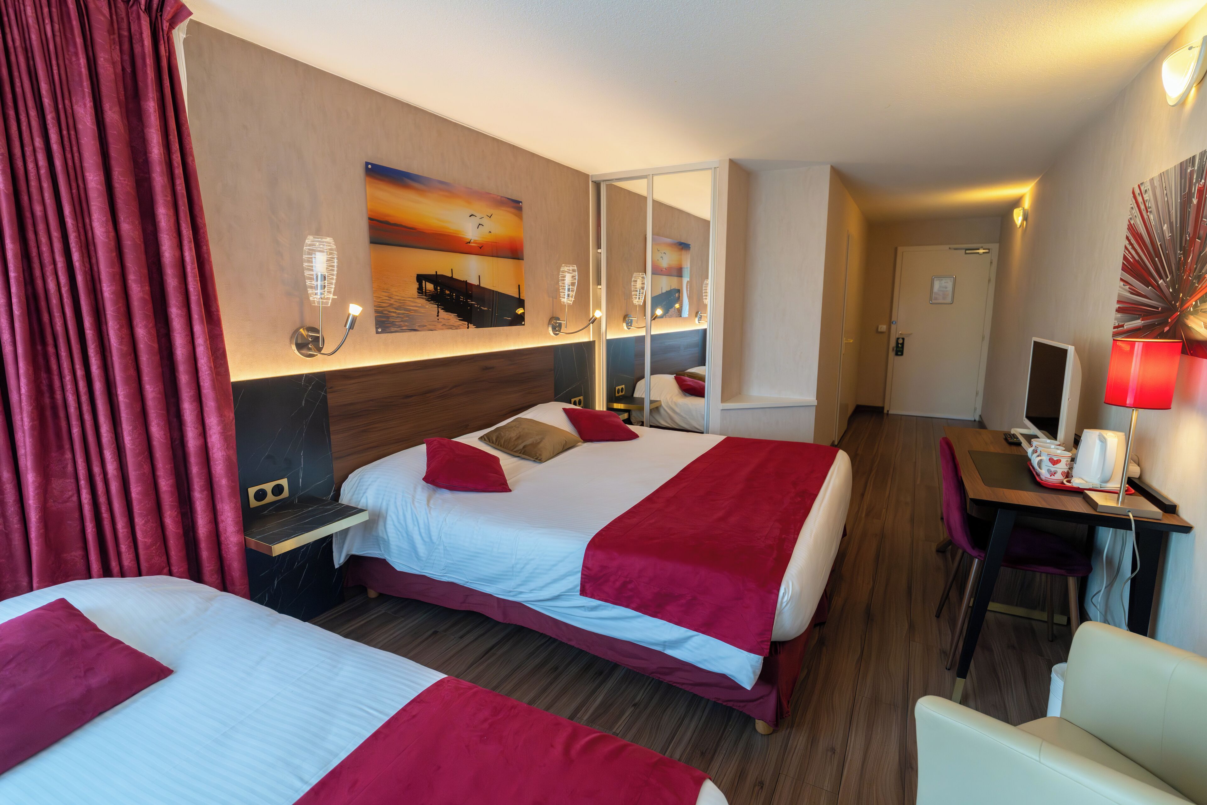 Ein Hotelzimmer mit zwei Betten, einem Schreibtisch, einem Stuhl, einem Fernseher und einem Spiegel.