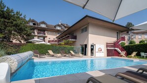 A swimming pool with lounge chairs and umbrellas, surrounded by buildings with balconies and a staircase. - Logis Hôtel Arc en Ciel (Thonon-les-Bains)