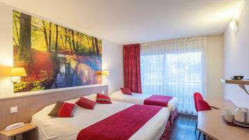 Habitación de hotel con dos camas, un escritorio, una silla, un cuadro de un bosque y una ventana con cortinas.
