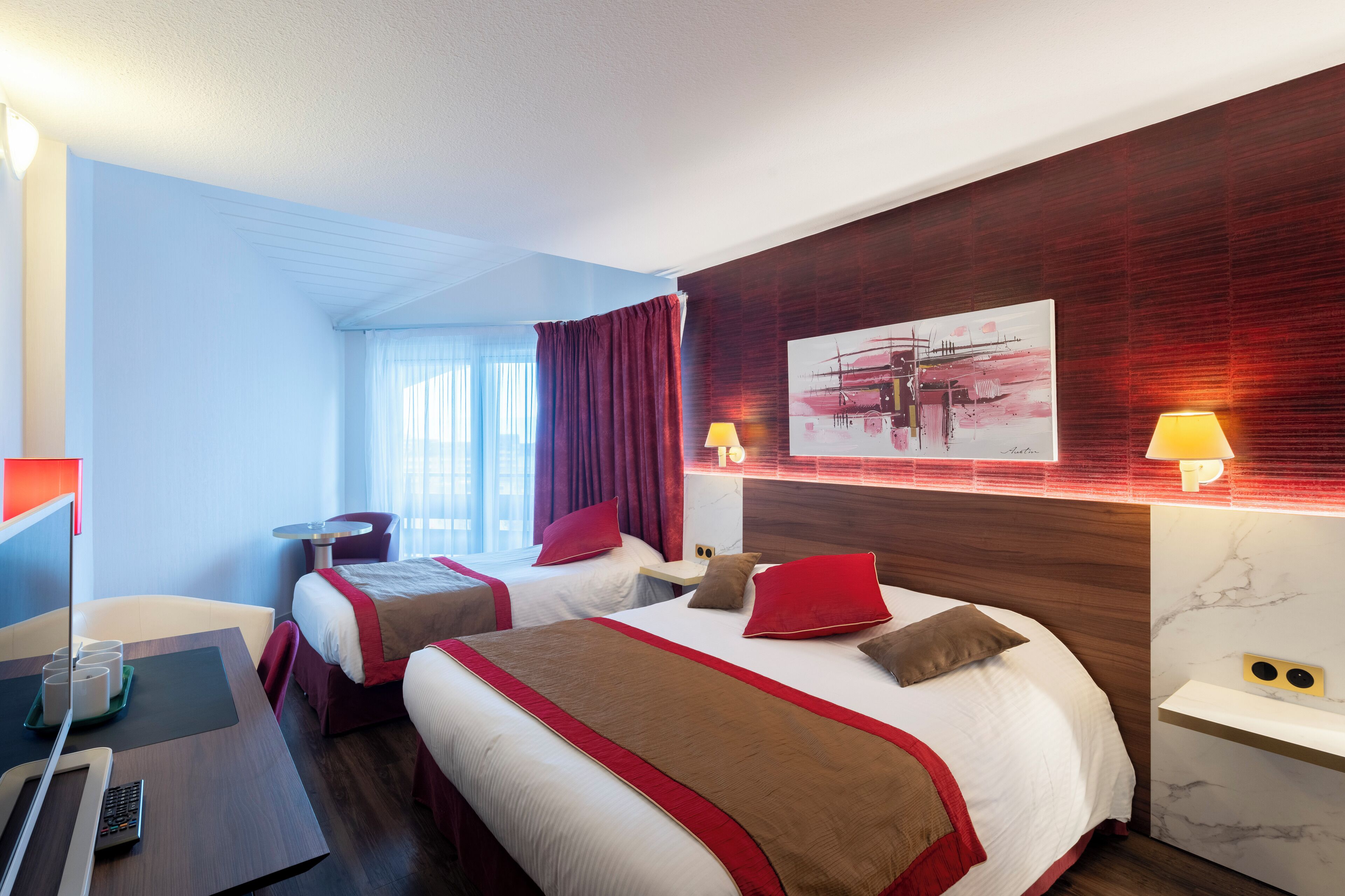Ein Hotelzimmer mit zwei Betten, einem Schreibtisch mit Computer und einem Fenster mit Vorhängen.