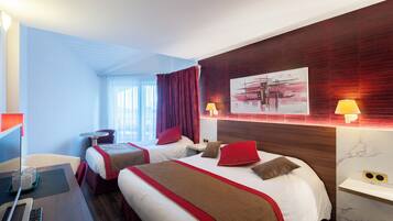 Ein Hotelzimmer mit zwei Betten, einem Schreibtisch mit Computer und einem Fenster mit Vorhängen.