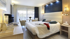 A hotel room with a large bed, bedside table, TV, and a small seating area with a table and chairs. - Logis Hôtel Arc en Ciel (Thonon-les-Bains)