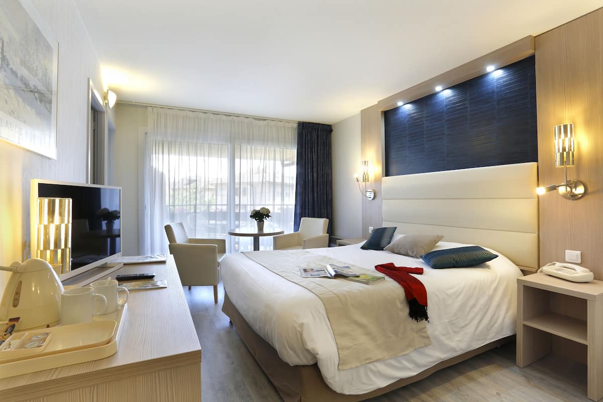 A hotel room with a large bed, bedside table, TV, and a small seating area with a table and chairs.
