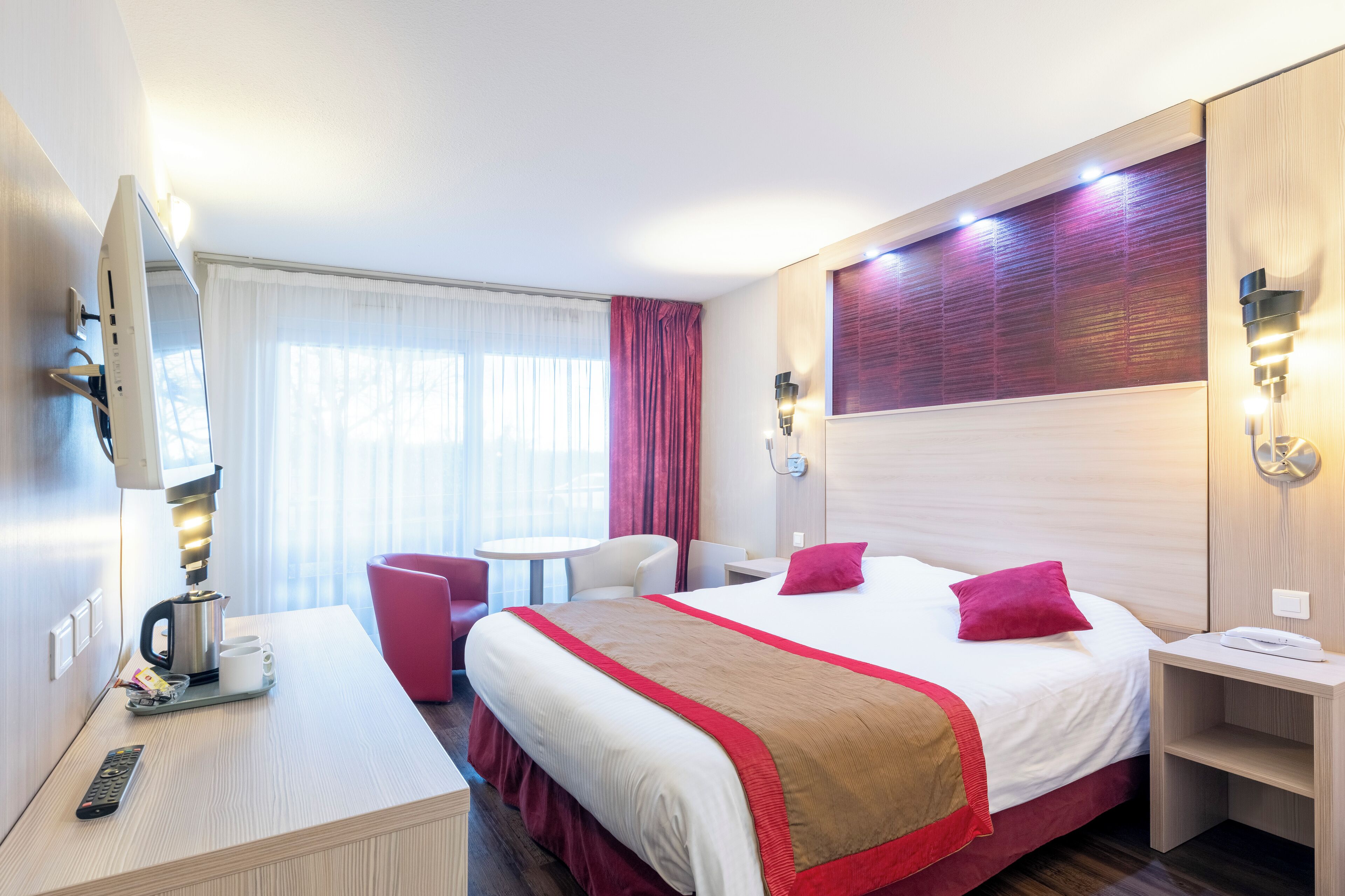 Una habitación de hotel con cama, mesita de noche, silla y escritorio con cafetera.