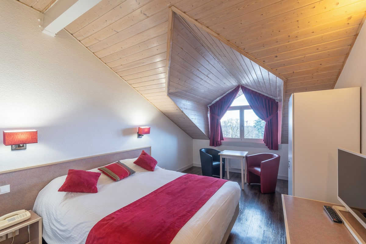 A hotel room with a large bed, a desk, a chair, a TV, and a window with curtains.