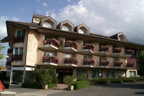 Un hotel de varios pisos con balcones decorados con jardineras, una entrada visible y un cielo despejado.