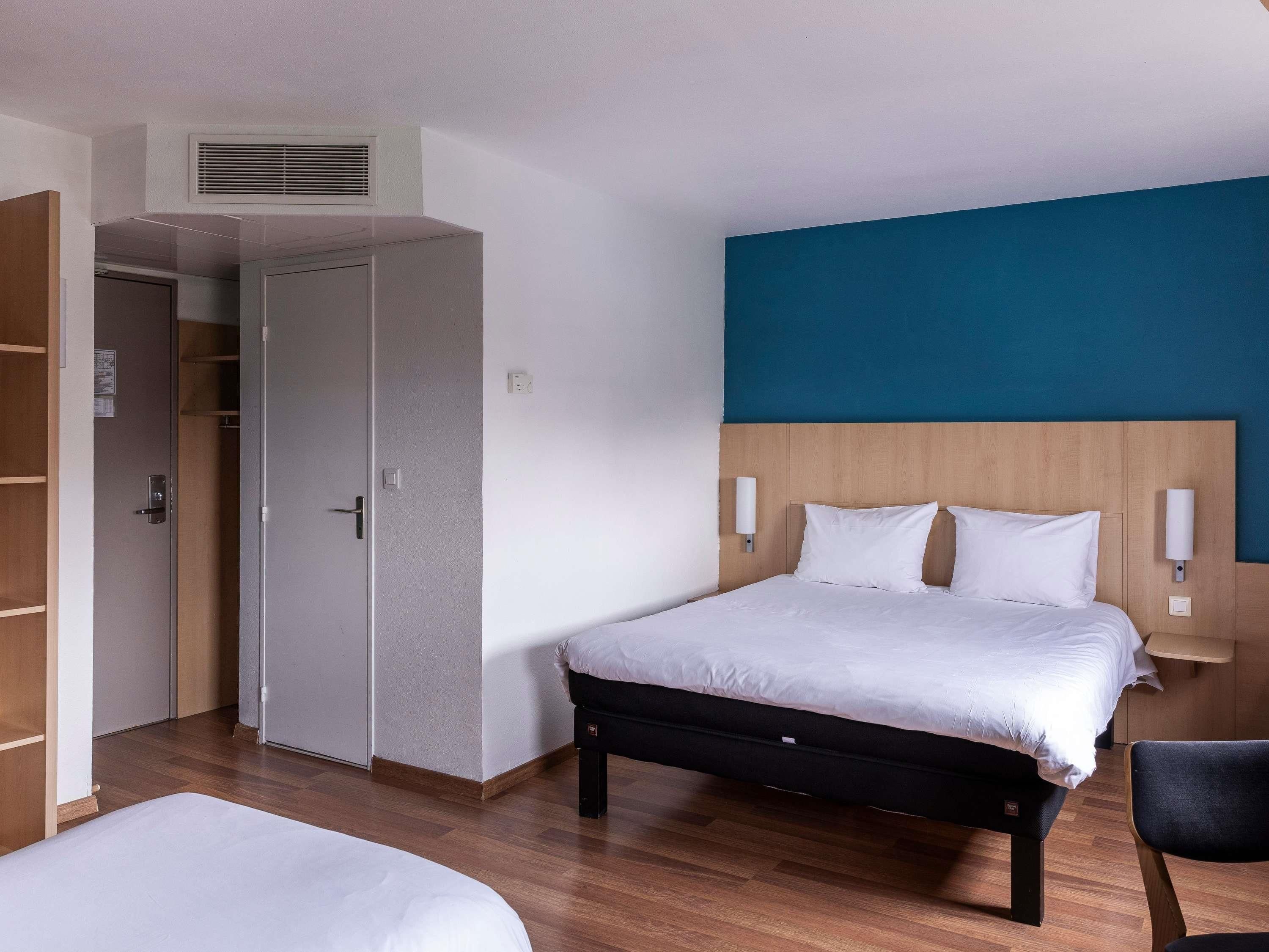 A hotel room with a bed, bedside tables, a wardrobe, and a small desk.