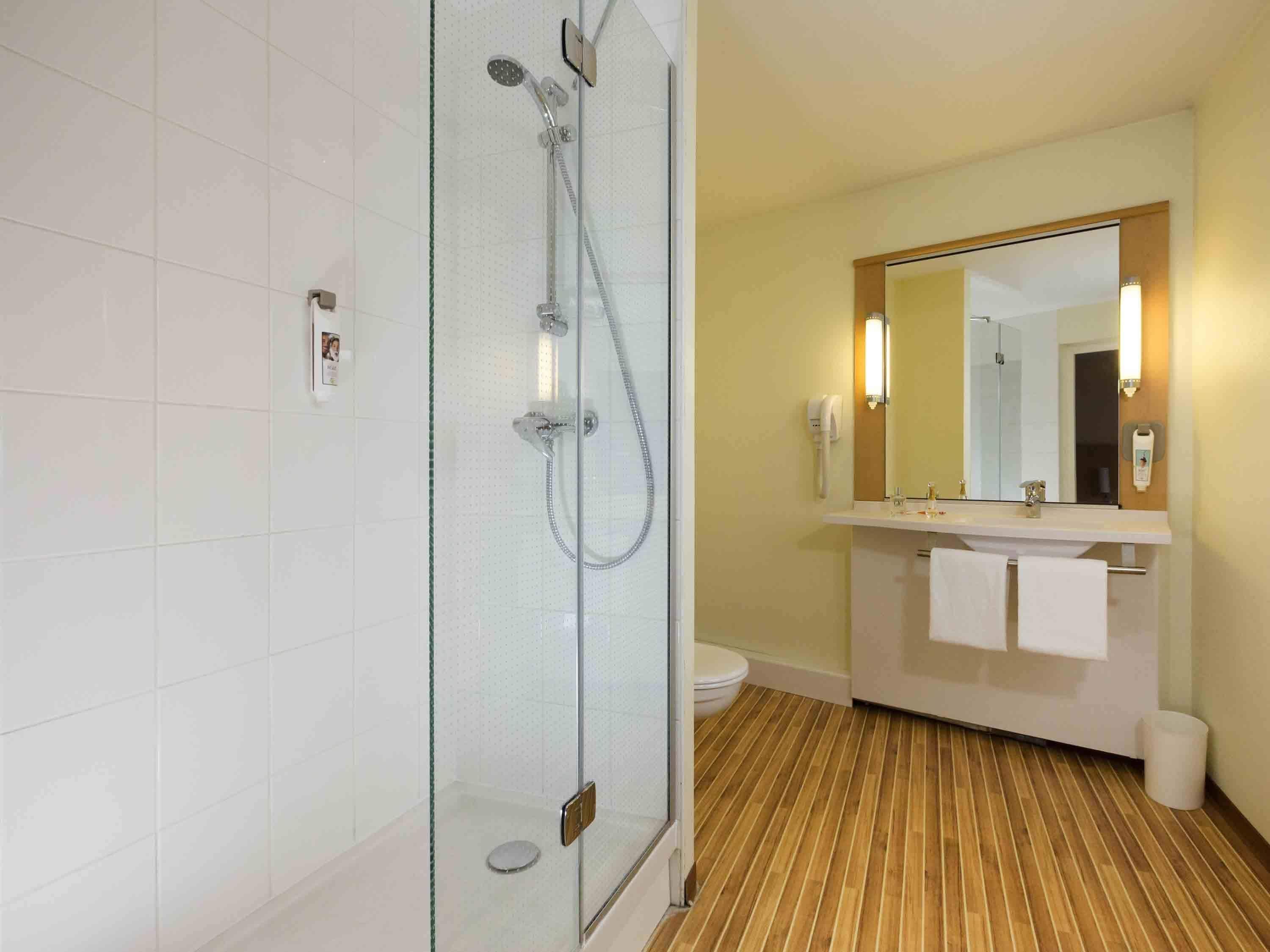 Un baño moderno con ducha de vidrio, piso de madera, lavamanos blanco con espejo y un inodoro.