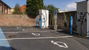 A parking area with electric vehicle charging stations, marked parking spaces, and a brick wall in the background. - ibis Lille Lomme Centre (Lille)
